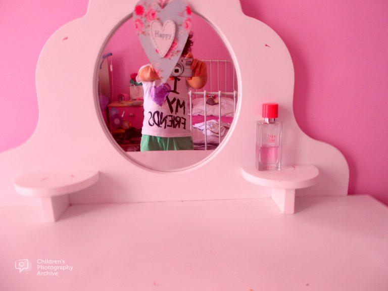 child's reflection in mirror face obscured by decorative heart making a self-portrait